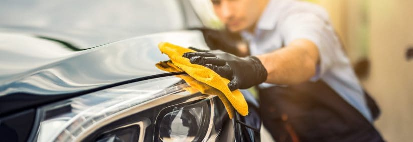 Person polishing a car's headlight with a yellow cloth.