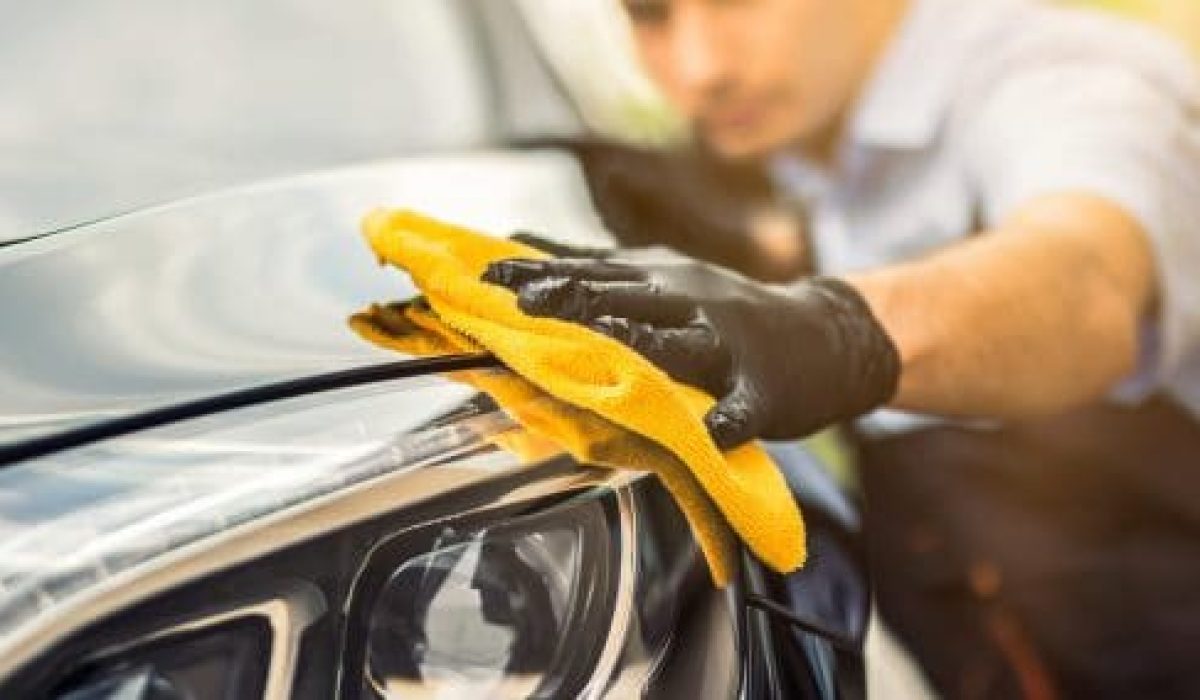 Person polishing a car's headlight with a yellow cloth.
